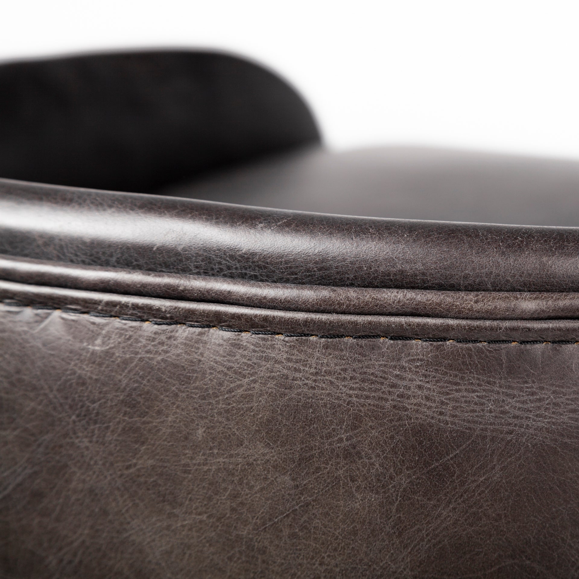 A modern bar stool featuring a curved brown leather seat cushion and backrest, supported by a slim gold-finished metal frame with a curved base, shown against a plain white background.