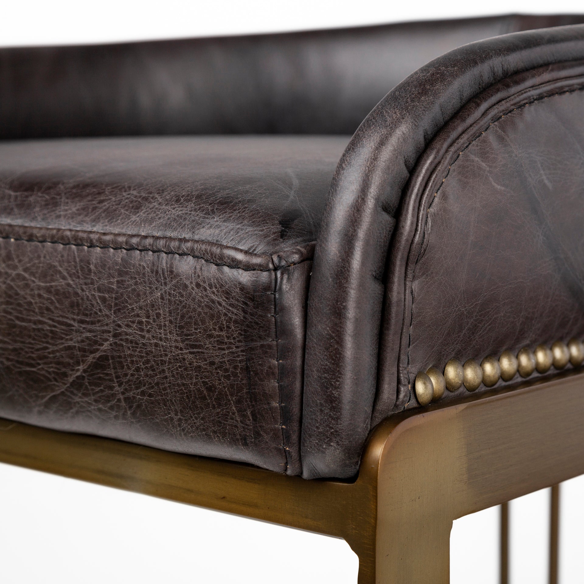 A modern bar stool featuring a curved brown leather seat cushion and backrest, supported by a slim gold-finished metal frame with a curved base, shown against a plain white background.
