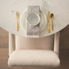 High-angle lifestyle shot featuring a complete place setting on the white marble surface with a neutral upholstered chair