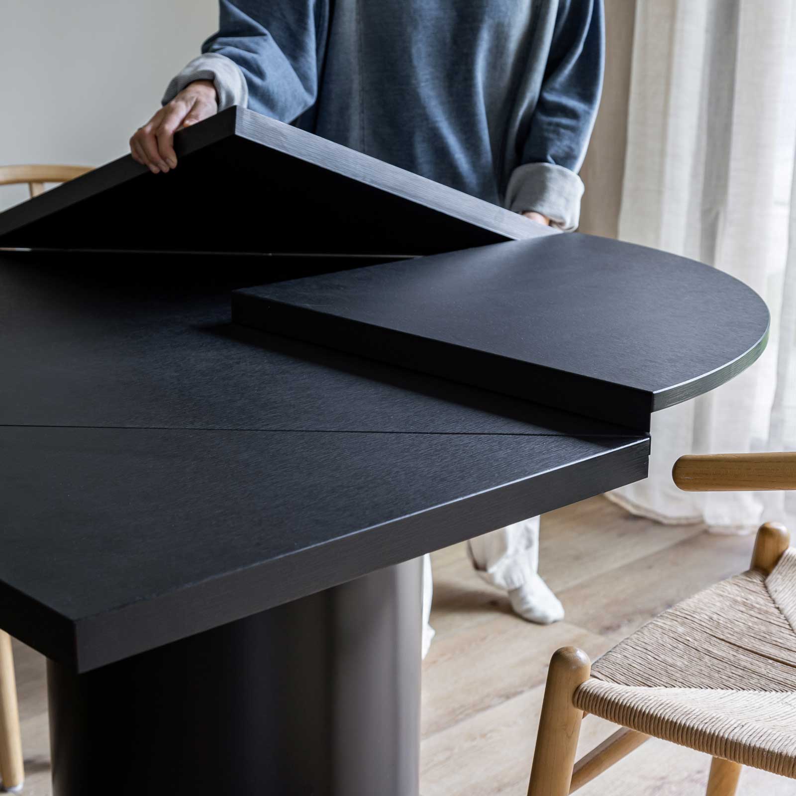 Front view of the Alter round dining table in a sleek black finish featuring a sturdy cylindrical pedestal base