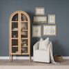 Lifestyle shot featuring the arched cabinet styled against a dark wall with framed art and a neutral accent chair