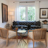 Lifestyle shot featuring the Astra table styled between two mid-century modern wooden armchairs in a bright living room
