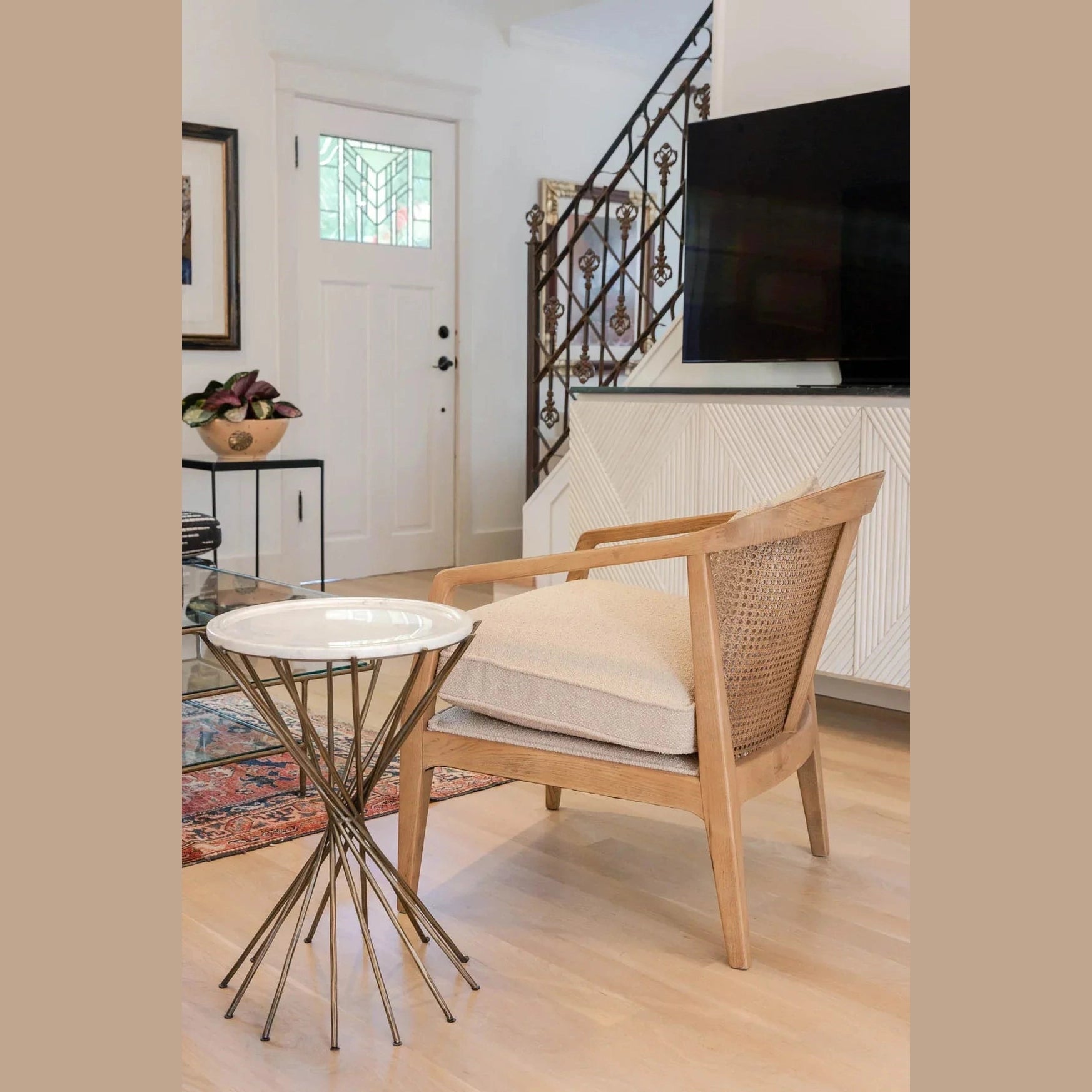 Lifestyle perspective demonstrating the table's scale next to a cane-back armchair in a modern home entryway
