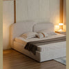 Three-quarter perspective view showcasing the soft architectural curves of the headboard and the plush upholstered base