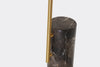 Close-up shot highlighting the slender brass support arm connected to the side of the dark veined marble pedestal