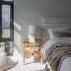 Close-up lifestyle shot of the bed headboard styled with a modern white table lamp and warm ambient lighting