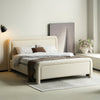 Lifestyle perspective of the upholstered bed under soft warm lighting highlighting the cozy texture of the neutral fabric