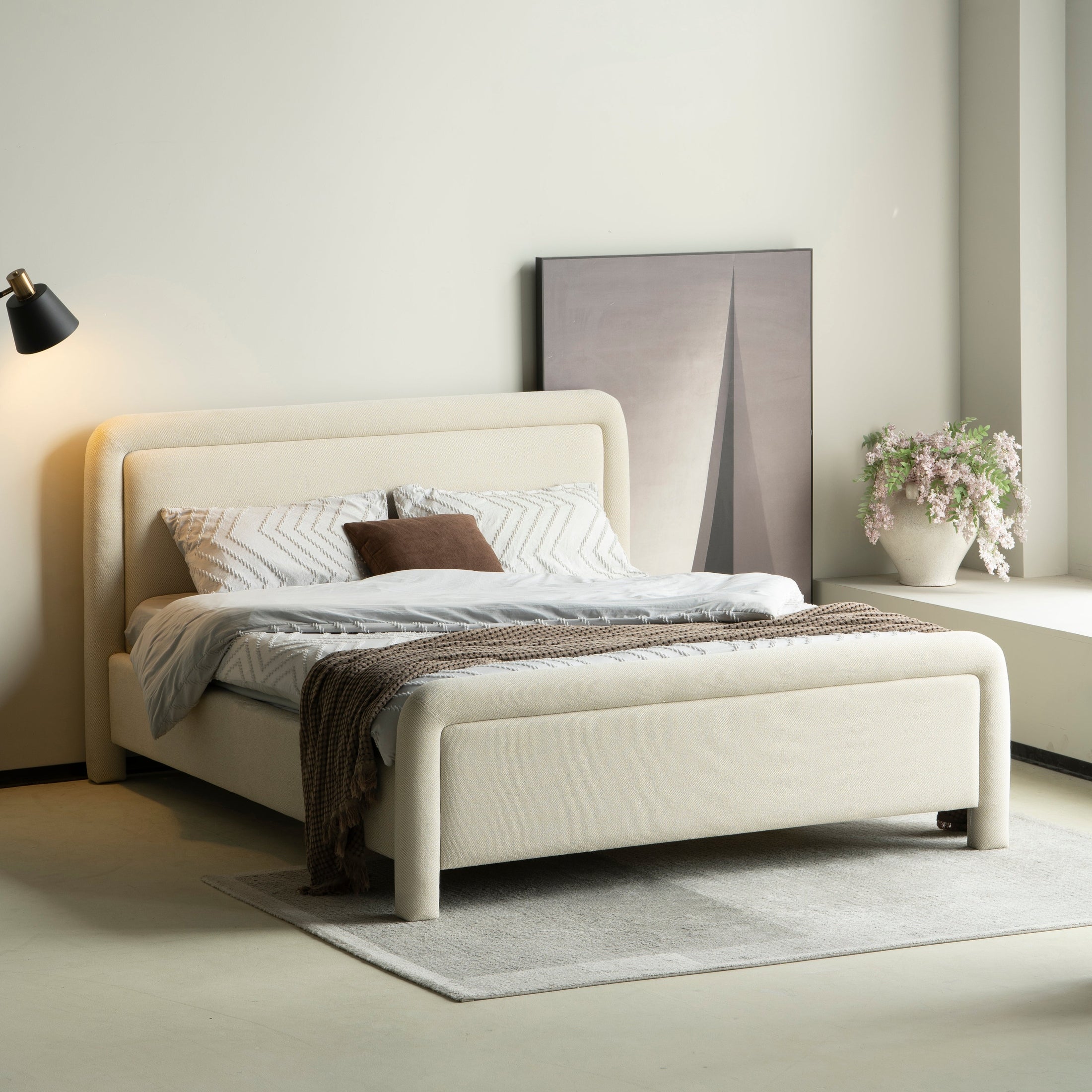 Lifestyle perspective of the upholstered bed under soft warm lighting highlighting the cozy texture of the neutral fabric