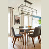 Real-home lifestyle shot featuring the dining table styled with dark grey chairs under a modern linear light fixture