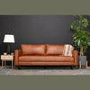Wide-angle lifestyle shot featuring the cane side table styled in a modern living room next to a cognac leather sofa