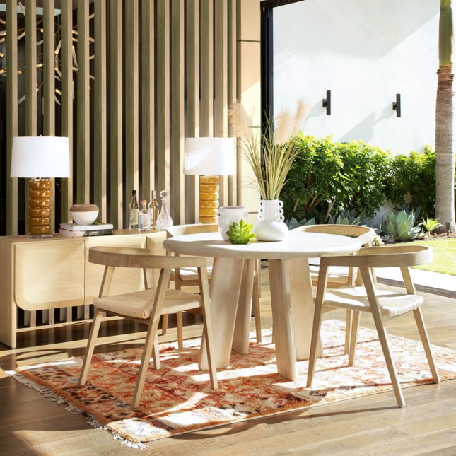 Lifestyle shot featuring the Alaia sideboard styled in a bright covered patio dining area with a matching round wood table and modern chairs