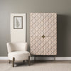 Lifestyle shot featuring the tall wood storage cabinet positioned next to a modern ivory armchair in a bright living room setting