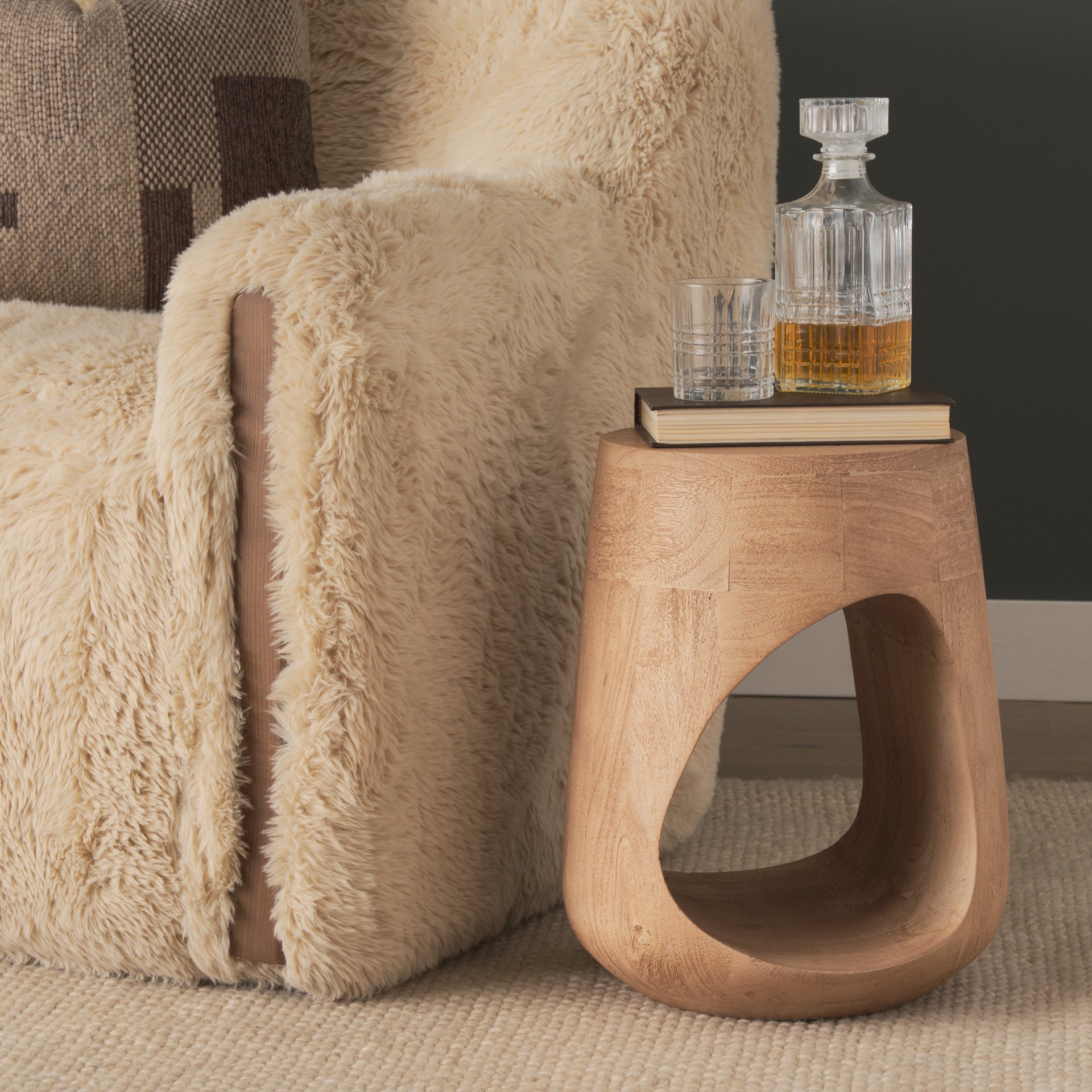 Lifestyle shot featuring the Cove table styled next to a textured cream armchair with a decanter and glass to show scale