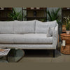 Wide lifestyle shot featuring the woven table paired with a contemporary grey sofa in a bright modern living space