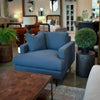 Lifestyle perspective of the drum table styled in a showroom setting next to a large blue upholstered armchair