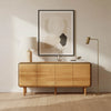 Lifestyle shot of a modern 4-door natural oak sideboard featuring rounded corners and a thin black perimeter inlay styled with a minimalist lamp and abstract art