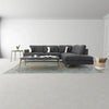 Wide lifestyle view showing the table paired with a large charcoal grey sectional sofa and a neutral area rug