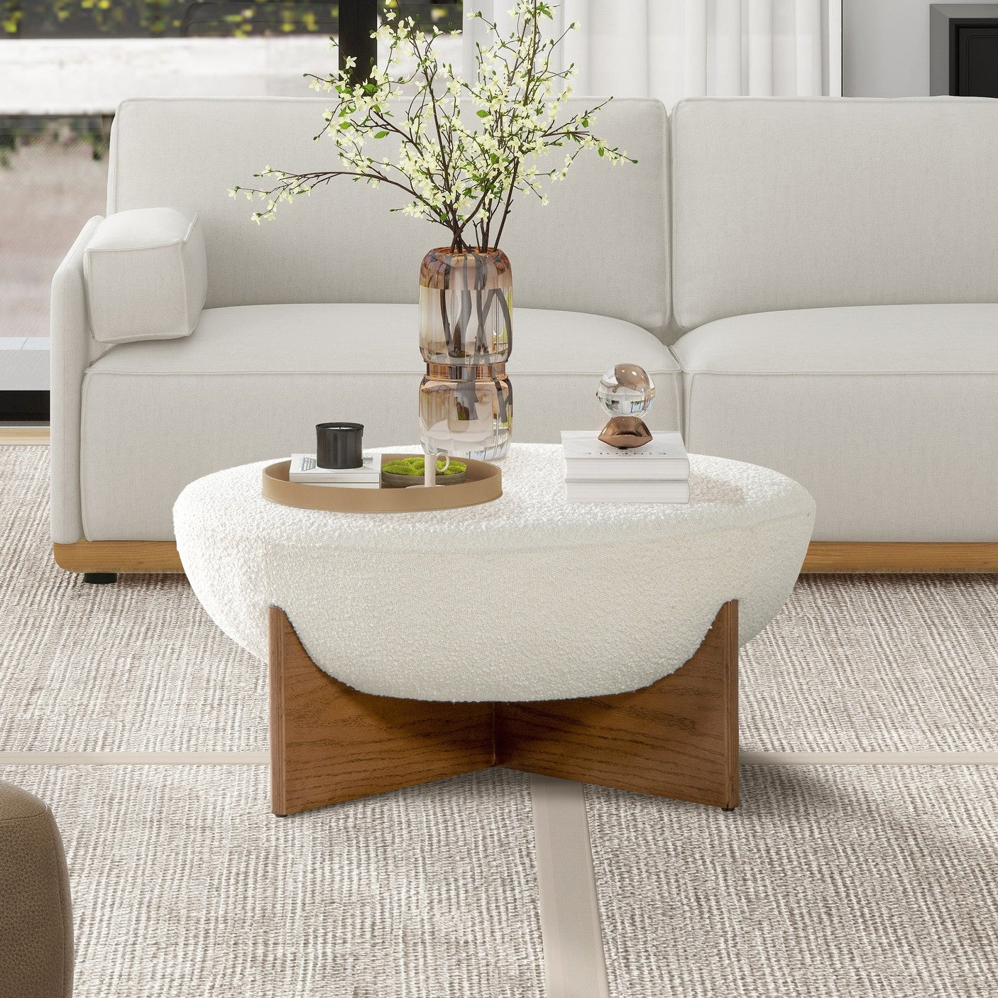 Front view of the Elara ottoman featuring a white bouclé bowl-shaped seat and a natural wood cross-base frame