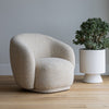 The Estelle armchair styled in a minimalist room setting next to a large potted indoor plant.
