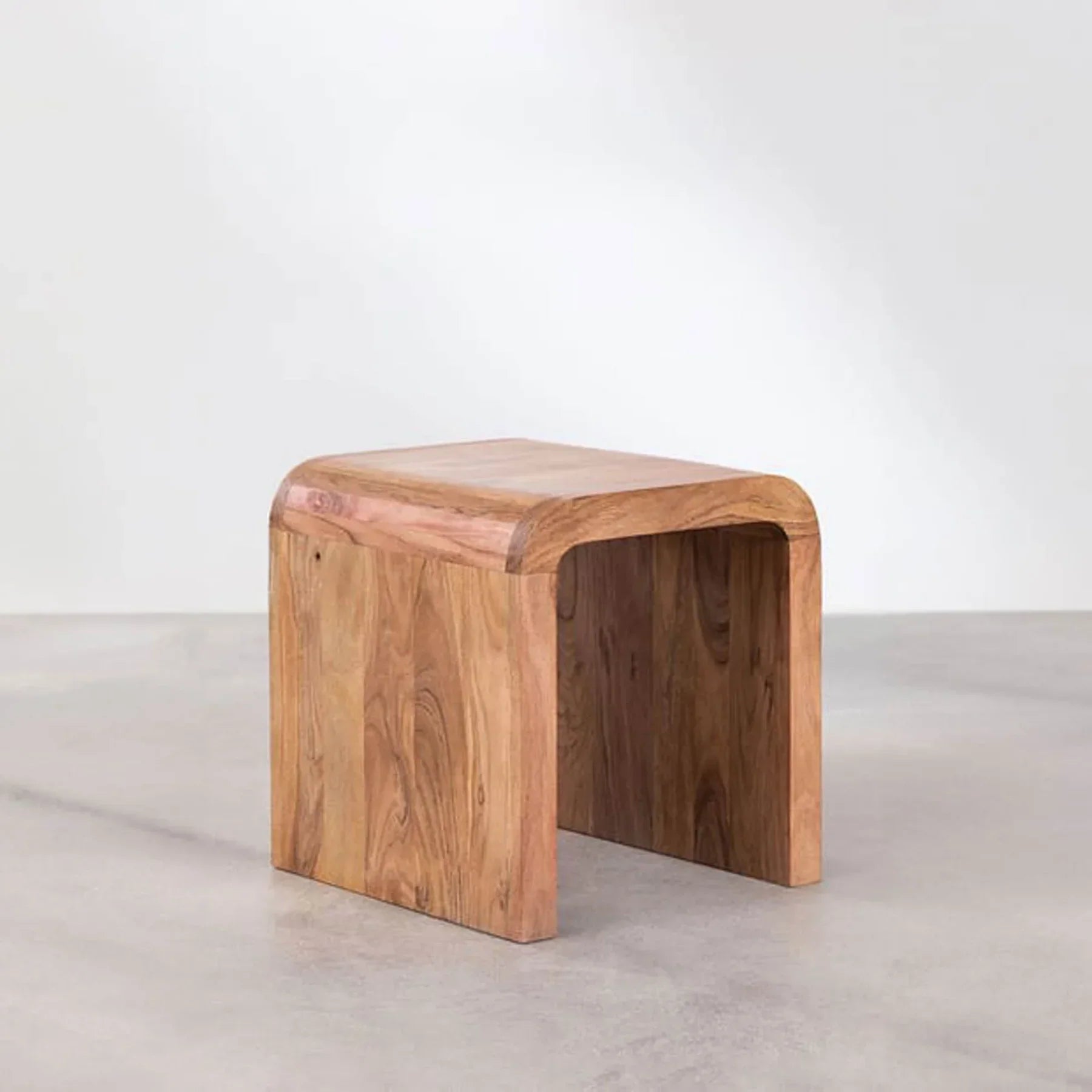 Three-quarter view of the Form Curve side table featuring a seamless waterfall edge design and rich natural wood grain in a U-shaped silhouette