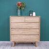 Wide lifestyle perspective showing the 5-drawer chest styled alongside a matching bed and nightstand against a deep teal wall