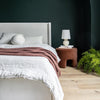Lifestyle shot of the chestnut velvet Ginger ottoman styled as a bedside accent in a contemporary bedroom
