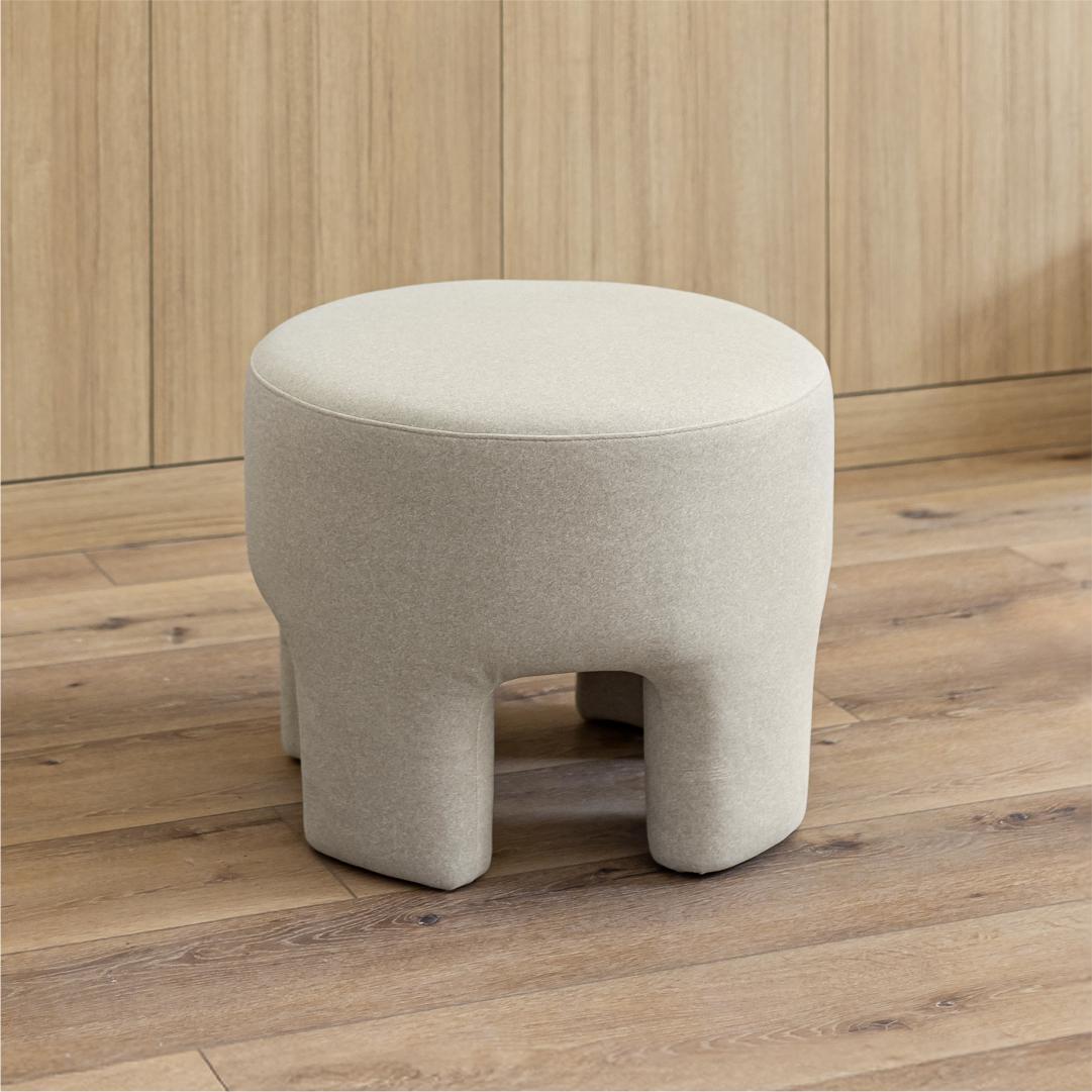 Studio shot showcasing the organic rounded top and architectural four-legged base of the natural velvet Ginger ottoman