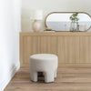 Lifestyle shot of the Ginger natural velvet ottoman styled in a modern interior setting near a wooden vanity
