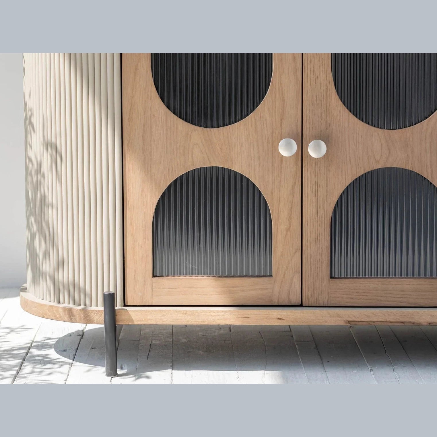 Macro shot focusing on the vertical grey fluted texture and the arched reeded glass door panels with white circular pulls