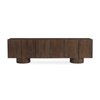 Front view of the Hadley media unit in warm brown solid wood featuring a seamless four-door design and architectural cylindrical plinth bases