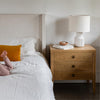 Studio lifestyle shot featuring the Hara 3-drawer dresser styled as a nightstand with a contemporary lamp in a bright bedroom setting