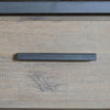 Macro detail shot focusing on the slim black metal handle and the textured natural oak wood grain of the drawer front
