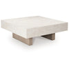 Three-quarter perspective highlighting the substantial square silhouette and the recessed plinth base of the Jorlaina table