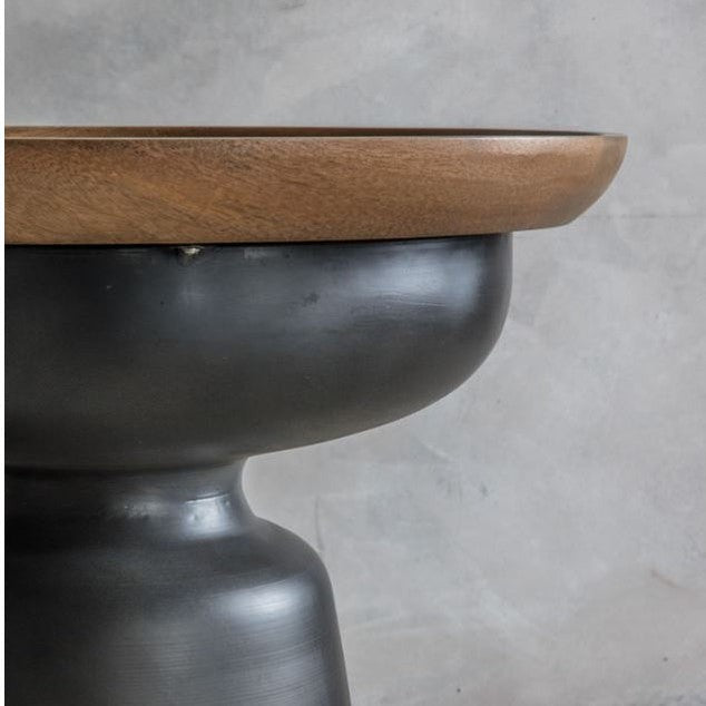 Front view of the Kana side table featuring a shallow natural mango wood bowl top on a tapered matte black metal pedestal base