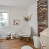 Lifestyle shot of the white boucle rocker in a cozy nursery setting with exposed brick and natural wood flooring