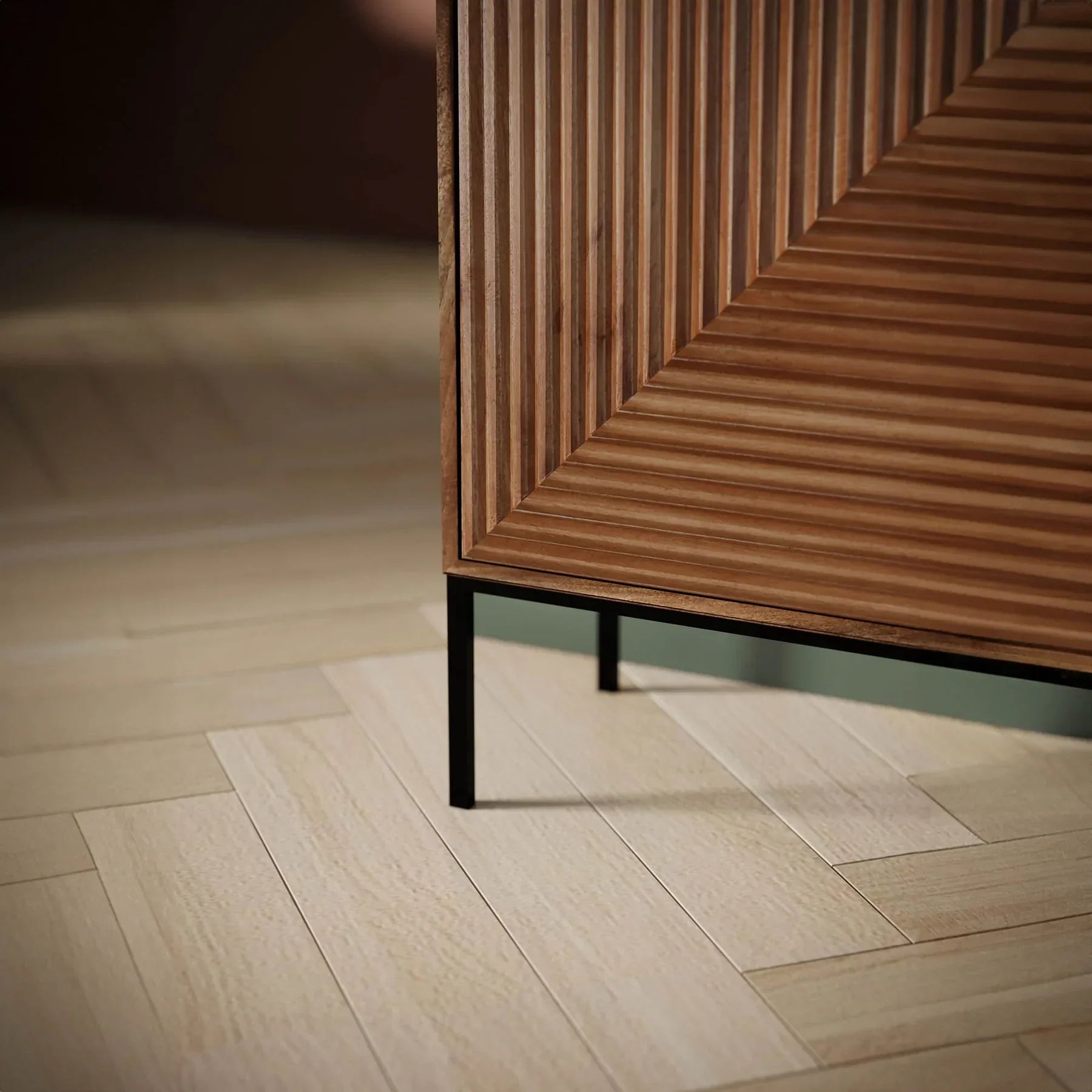Front view of the Nikita sideboard featuring a warm wood finish with intricate chevron-patterned ribbed door panels and slim black metal legs