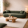 Dark grey boucle curved sofa styled in a modern living room with round wooden coffee table, rug, and warm neutral decor