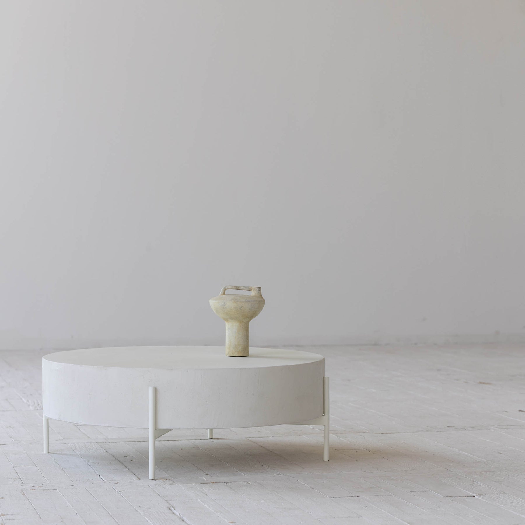 Front view of the Luna coffee table featuring a thick circular drum-style top in white concrete supported by a minimalist four-leg metal base