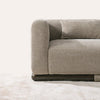 Side view detail of Malakai sofa armrest with taupe textured fabric upholstery and curved dark wood base frame