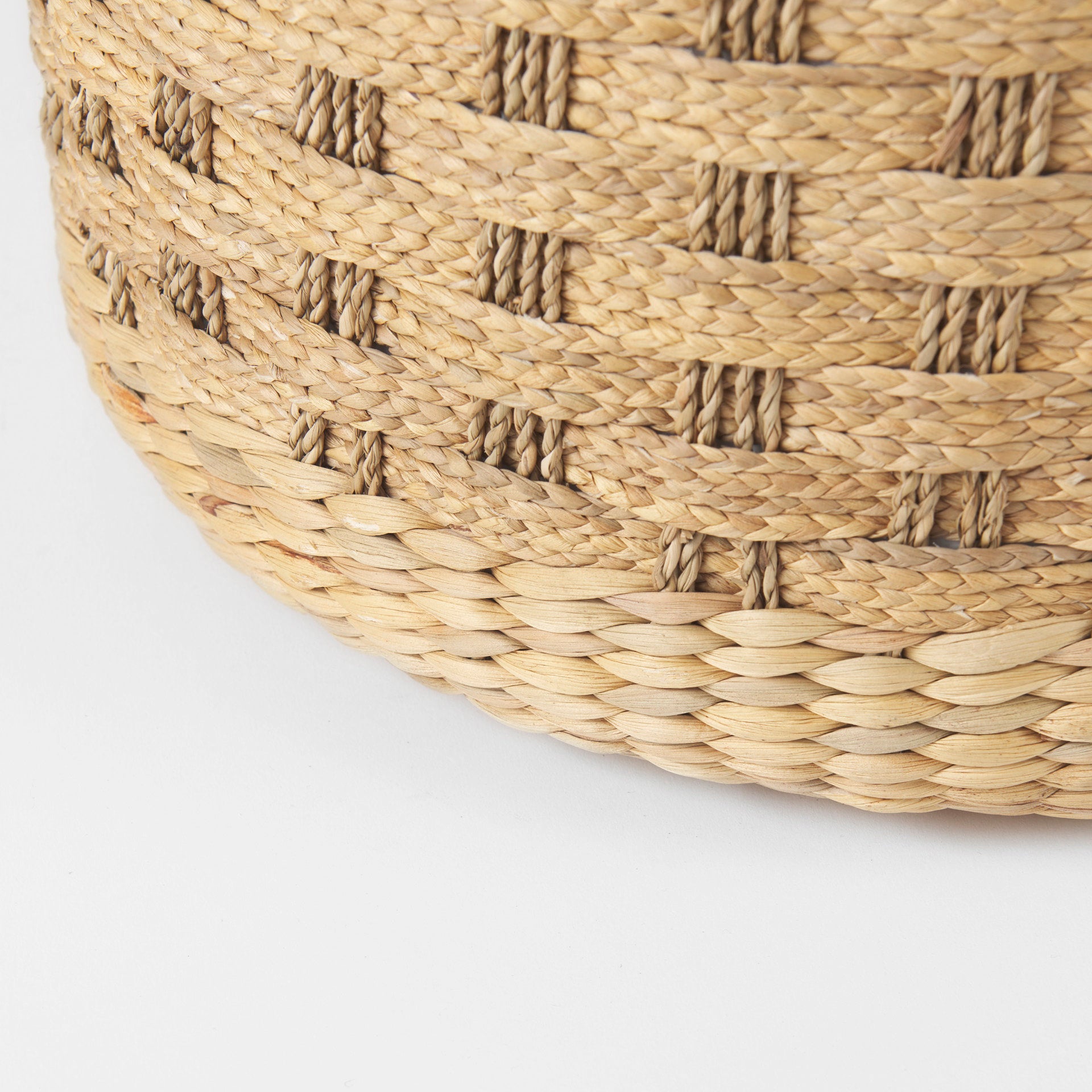 Front three-quarter view of the Michelle round pouf featuring a decorative checkered woven seagrass design in light brown