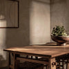 Perspective lifestyle shot featuring the wooden table in a minimalist setting with natural light and simple floral decor
