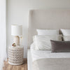 Close-up perspective of the headboard styled with a white table lamp and textured neutral bedding