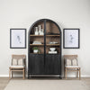 Lifestyle shot featuring the black arched cabinet styled with books and ceramics between two minimalist chairs