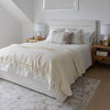 Lifestyle view of the bed styled on a light gray rug with layered neutral blankets and artistic decor