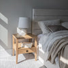Lifestyle shot featuring the Julia bed styled with neutral linens and an oak nightstand in a bright contemporary room