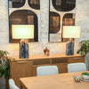 Lifestyle shot featuring the natural oak sideboard styled with two large table lamps and abstract art in a warm dining setting