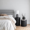 Lifestyle shot featuring the bed styled with dark charcoal accents and a black minimalist side table