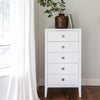 Studio lifestyle shot featuring the white tall dresser styled with a decorative vase in a bright, airy bedroom corner