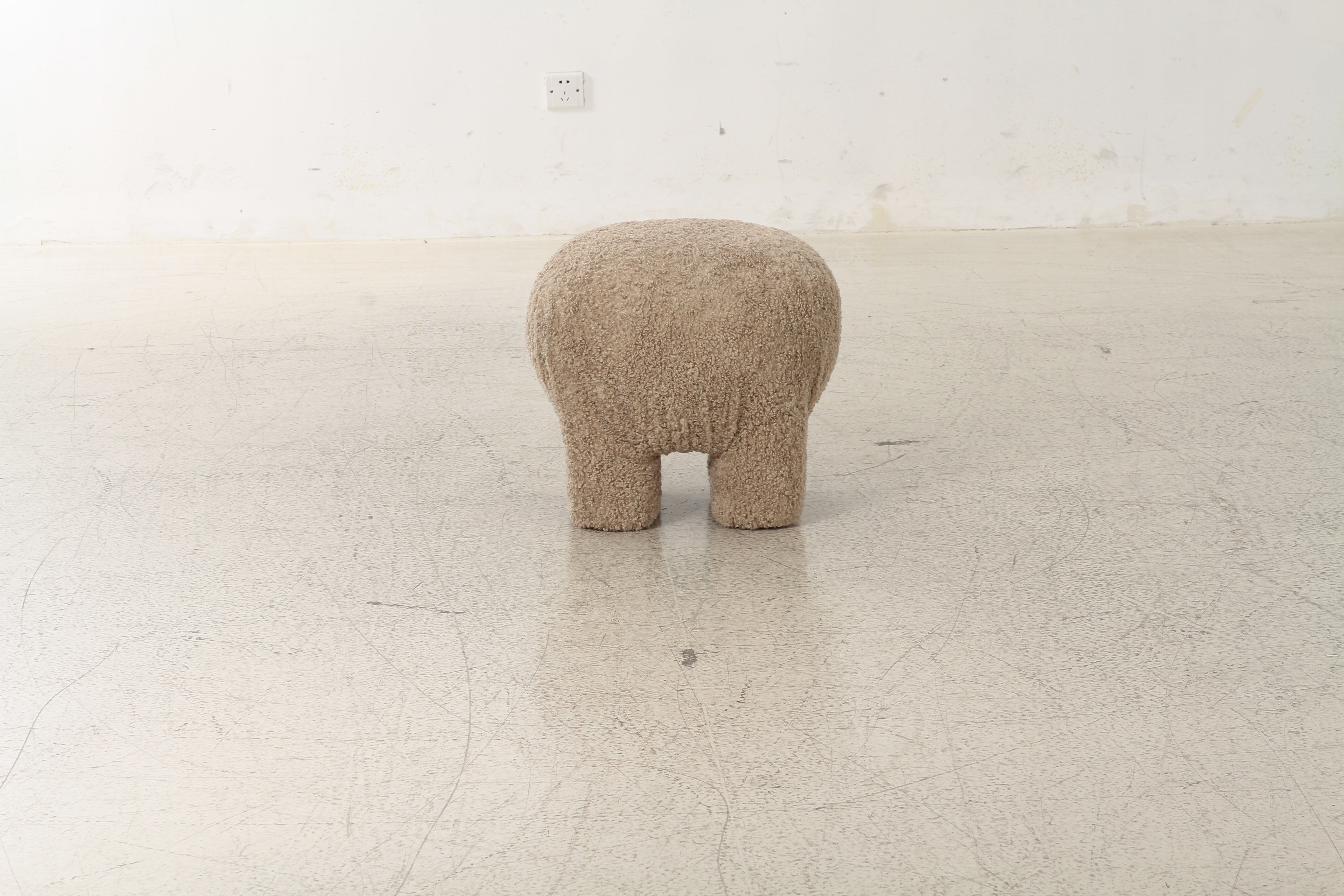 Front view of the Moin upholstered ottoman in taupe curly bouclé featuring a playful four-legged sculptural silhouette
