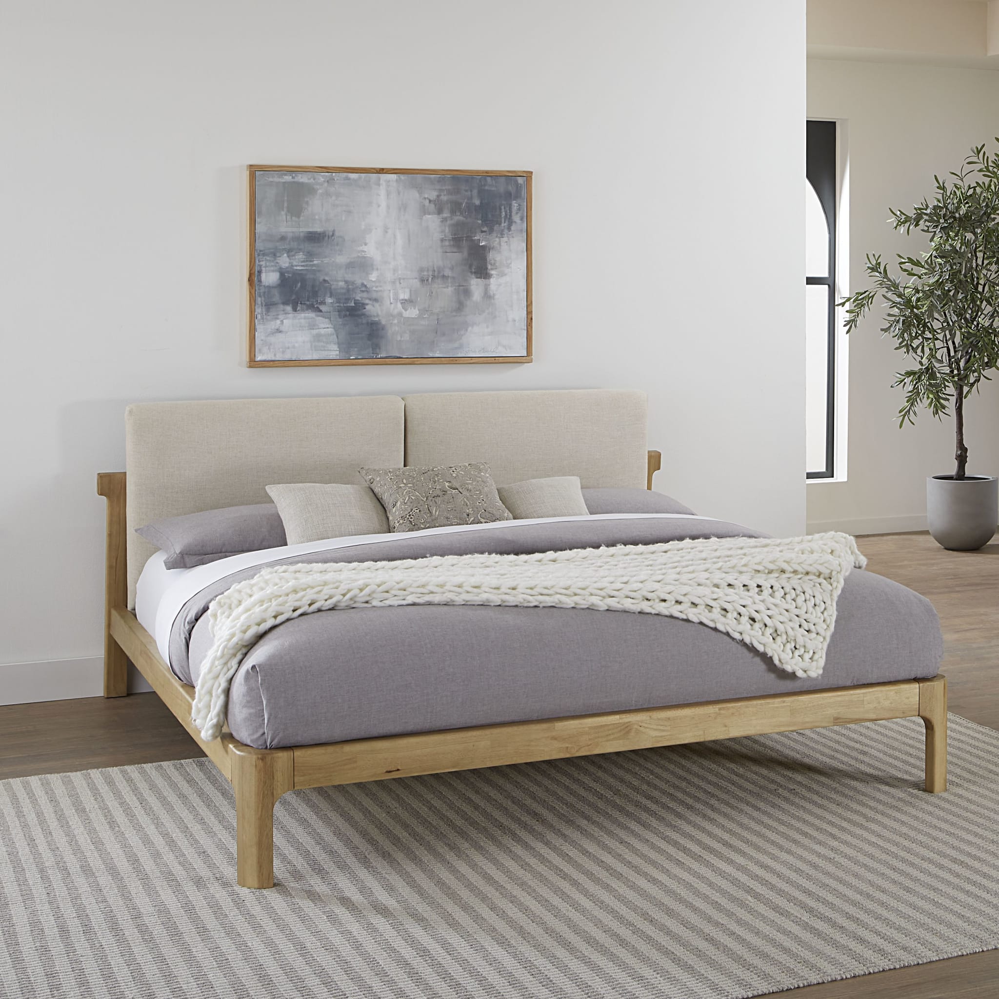Front view of the Havn platform bed featuring a ginger-finished ash wood frame and a two-cushion natural linen headboard